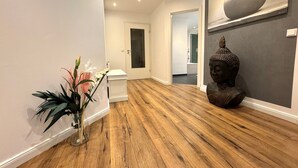 Un couloir avec un plancher en bois, une porte blanche, une statue et un vase rempli de fleurs.