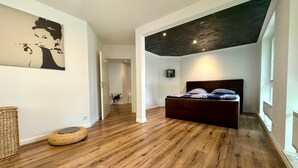 Une chambre à coucher avec un lit, un plancher en bois, un plafond sombre et un couloir menant à une autre pièce.
