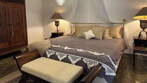 A bedroom with a bed, bedside lamps, a wooden wardrobe, and a bench.
