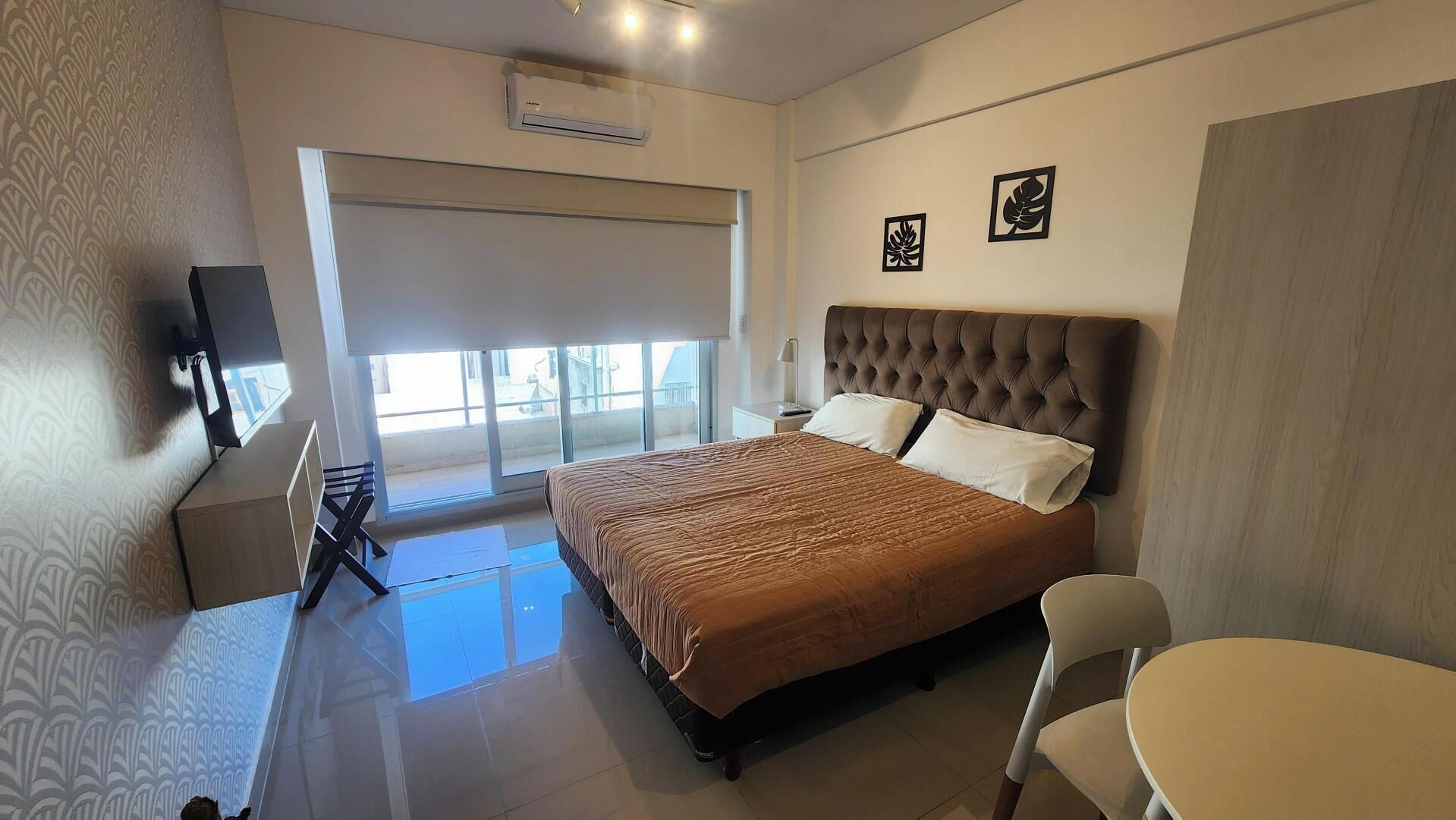 A hotel room with a bed, a desk, a chair, a TV, and a balcony with a view.