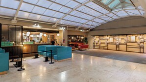 Eine geräumige Lobby mit hoher Decke und Oberlichtern, Sitzbereichen, einem Empfangsbereich und einer Wand mit verschiedenen Ausstellungsstücken.