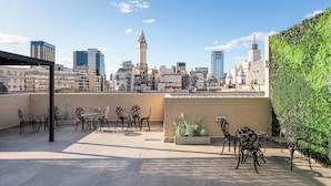 Eine Dachterrasse mit Außenbestuhlung, einem Glockenturm und einer Stadtansicht im Hintergrund.