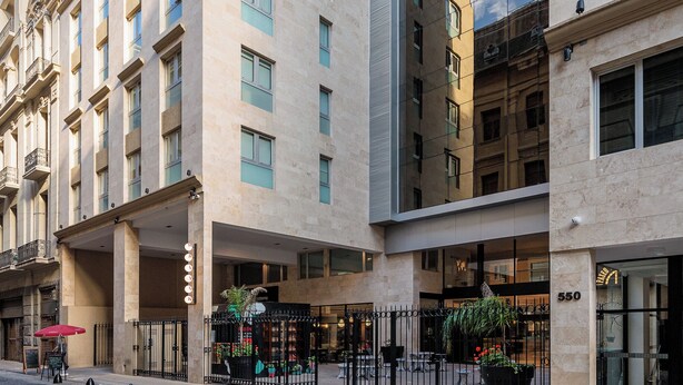 Ein mehrstöckiges Hotel mit moderner Fassade, großen Fenstern und einem gepflasterten Innenhof mit Leitpfosten.