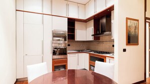 A modern kitchen with white cabinets, a stainless steel oven, a gas stove, and a wooden dining table. - Umbertina Cozy Apartment by Wonderful Italy (Bari)