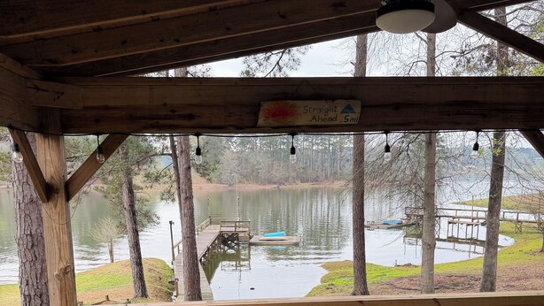 A wooden deck with a round table and two chairs, overlooking a lake with docks and a wooden pier. - WATERFRONT with private dock ,boat ramp, paddle boats and Kayaks!! (Many)
