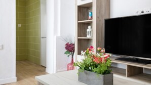 Een moderne woonkamer met een flatscreen televisie, een grijze vaas met bloemen en een houten kast.