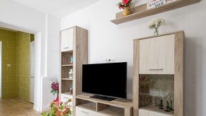 Een moderne woonkamer met een flatscreentelevisie, houten kasten en een klein plankje met decoratieve objecten.