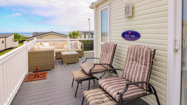A deck with wicker furniture and striped chairs, a sign reading "Park Lane", and a view of the sea. - Ty Seren (New Quay)
