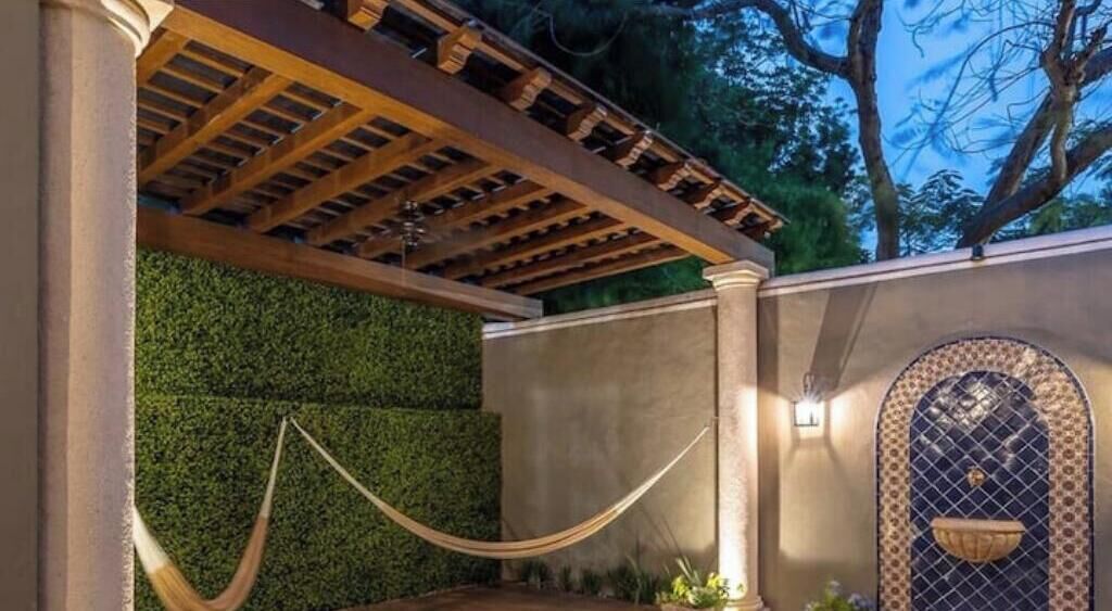 Un espace extérieur abrité, doté d’une pergola en bois, d’un hamac et d’un mur décoratif agrémenté d’une arche ornée.