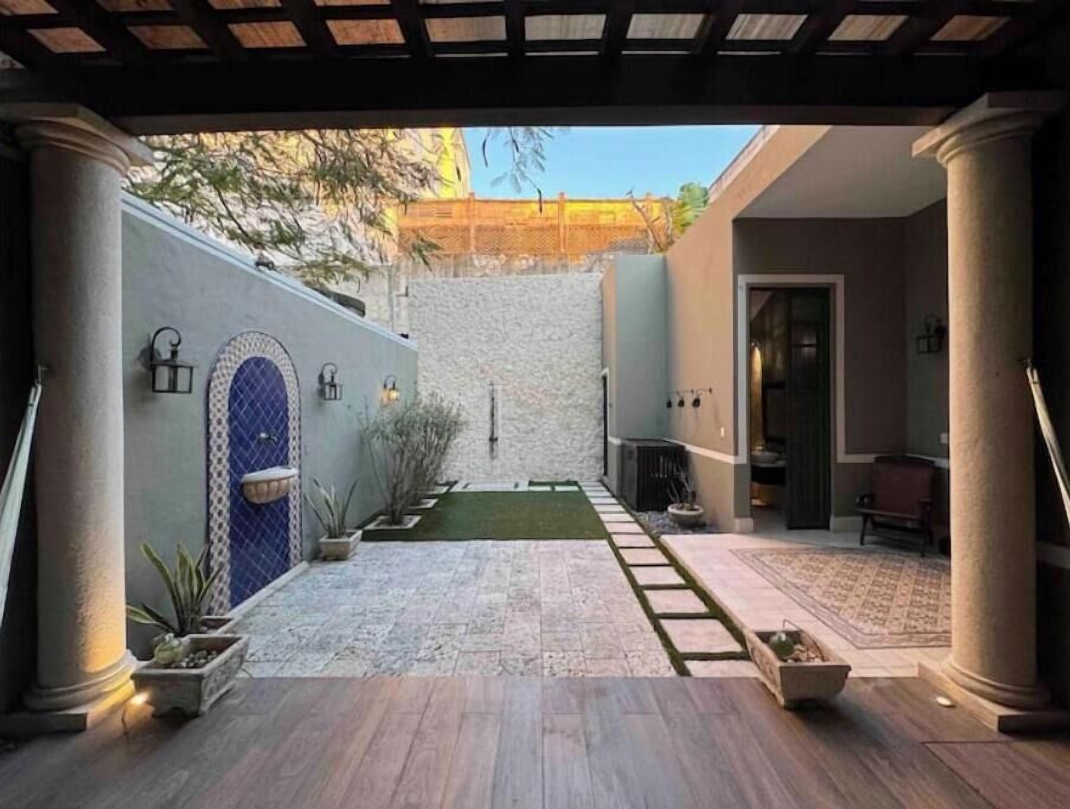 Un patio con piso de baldosas, un pequeño jardín y una puerta que da a una habitación.