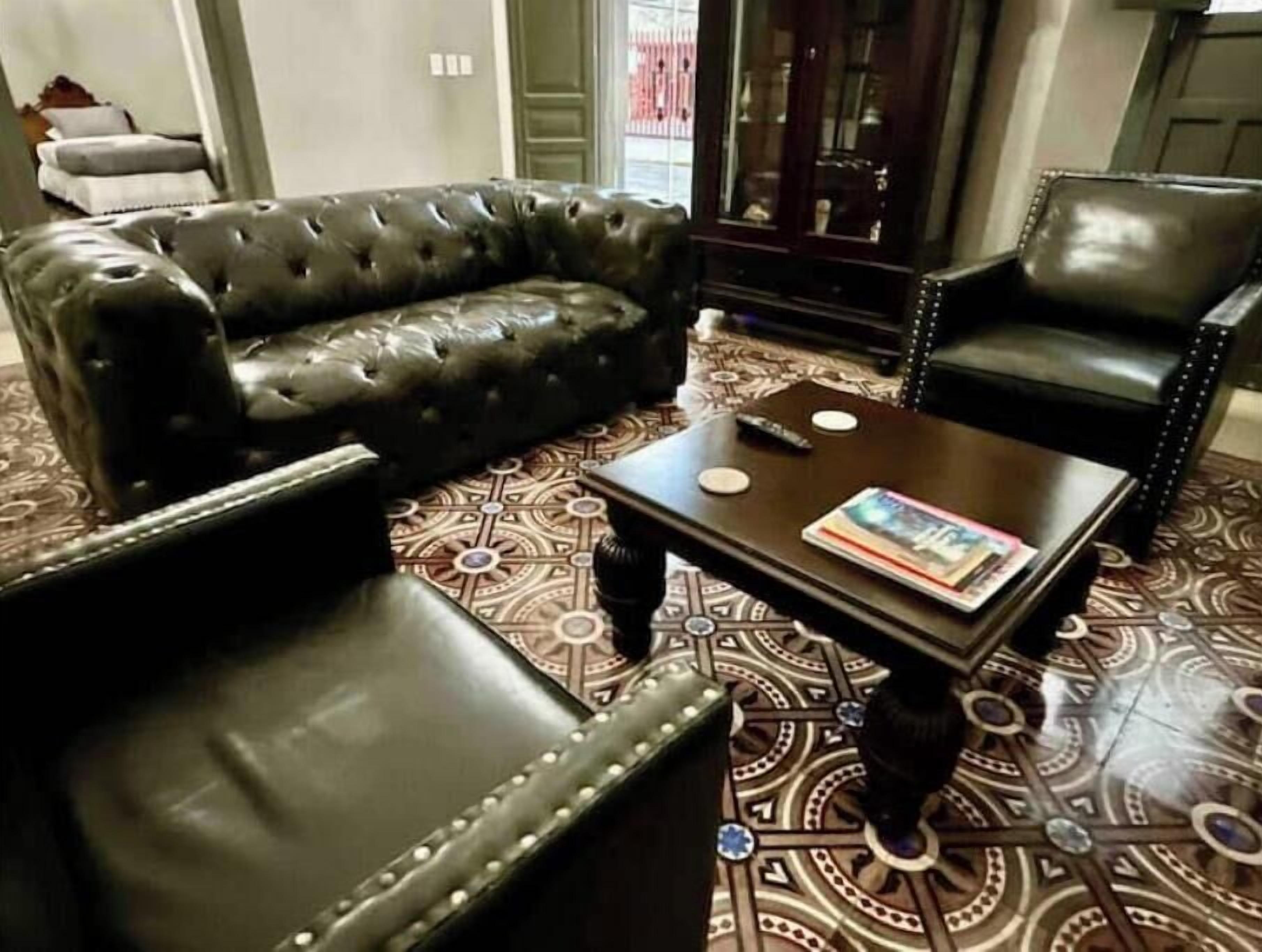 A room with a black leather sofa, a matching armchair, and a small coffee table with magazines.