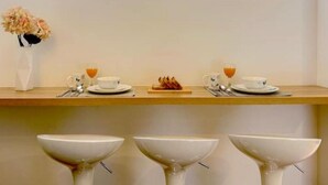 En morgenmadsopstilling med to kopper te, et lille frugtfat og en vase med blomster på et træbord.