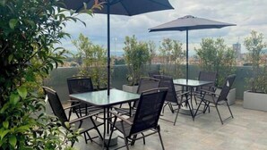 En udendørs patio med borde og stole, omgivet af krukker med planter og parasoller.