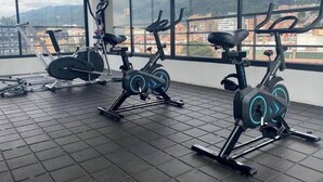 Et træningscenter med motionscykler og en romaskine, store vinduer med udsigt til et bjerglandskab.