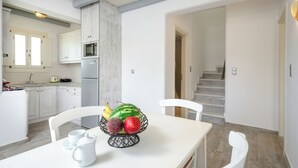 A modern kitchen with white cabinets, a dining table with a fruit bowl, and a staircase leading to another level. - My Villa, 2-bedroom villa in gorgeous Naxos with AC, WiFi (Naxos)