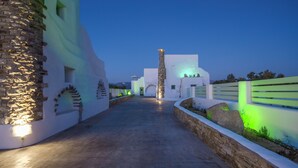 A pathway leading to a building with white walls and stone accents, a stone column, and green lighting. - My Villa, 2-bedroom villa in gorgeous Naxos with AC, WiFi (Naxos)