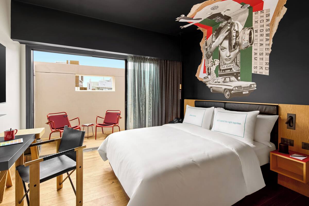Een hotelkamer met een groot bed, een bureau met stoel, een bijzettafeltje en uitzicht buiten door een schuifdeur.