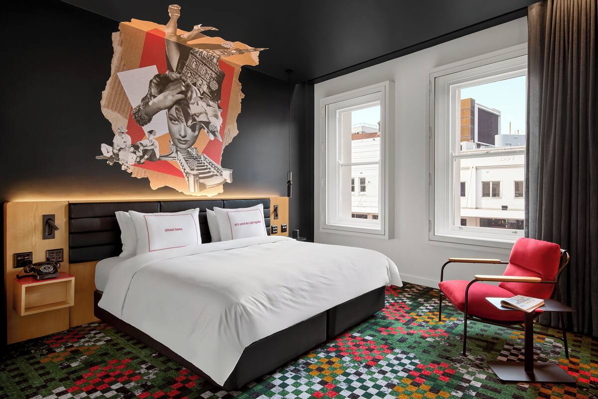 Hotelkamer met een groot bed, een rode fauteuil, een kamerbreed tapijt met een patroon en een muur met een verouderd effect.