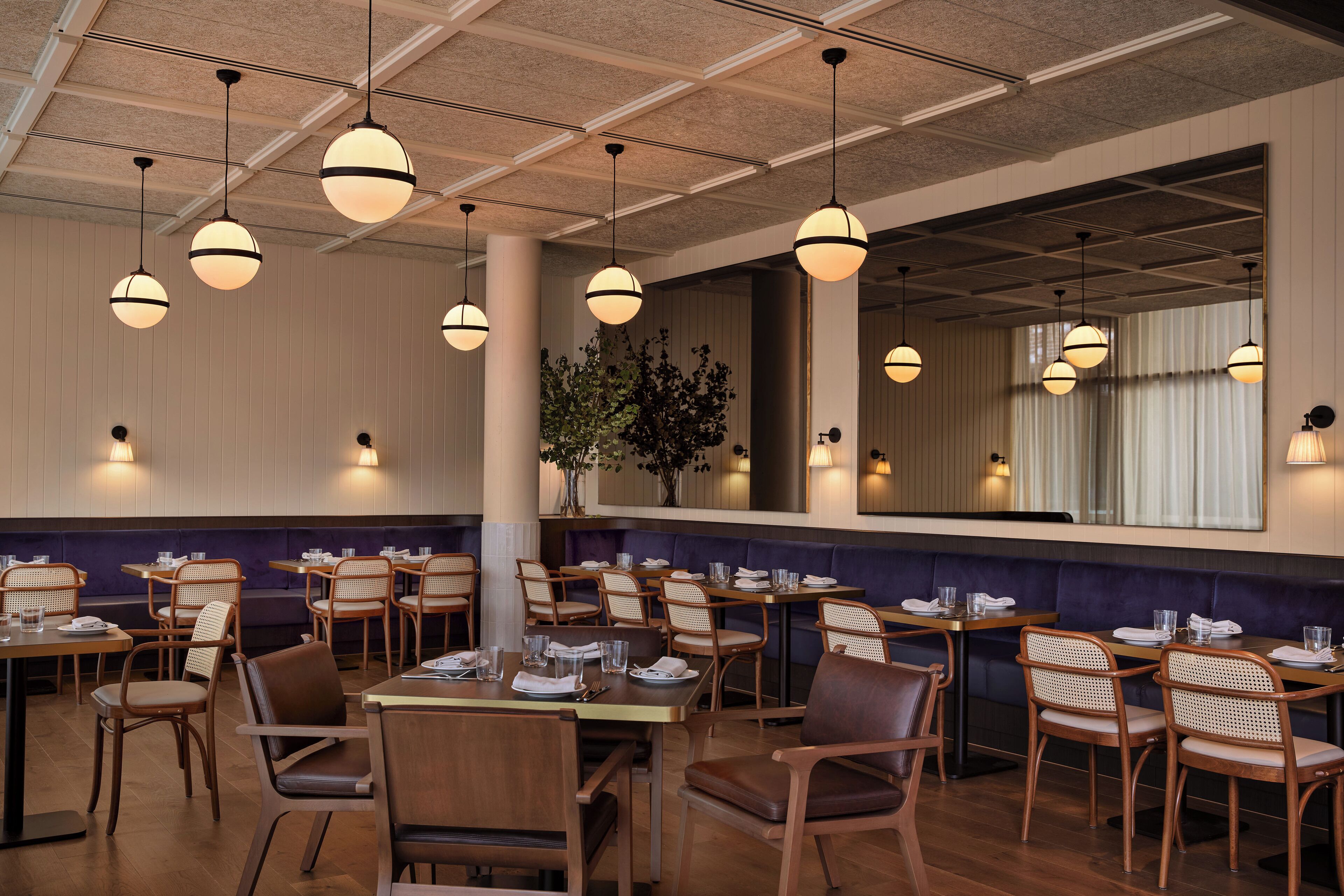 Un restaurant avec des tables et des chaises en bois, des lampes suspendues et un grand miroir au mur.