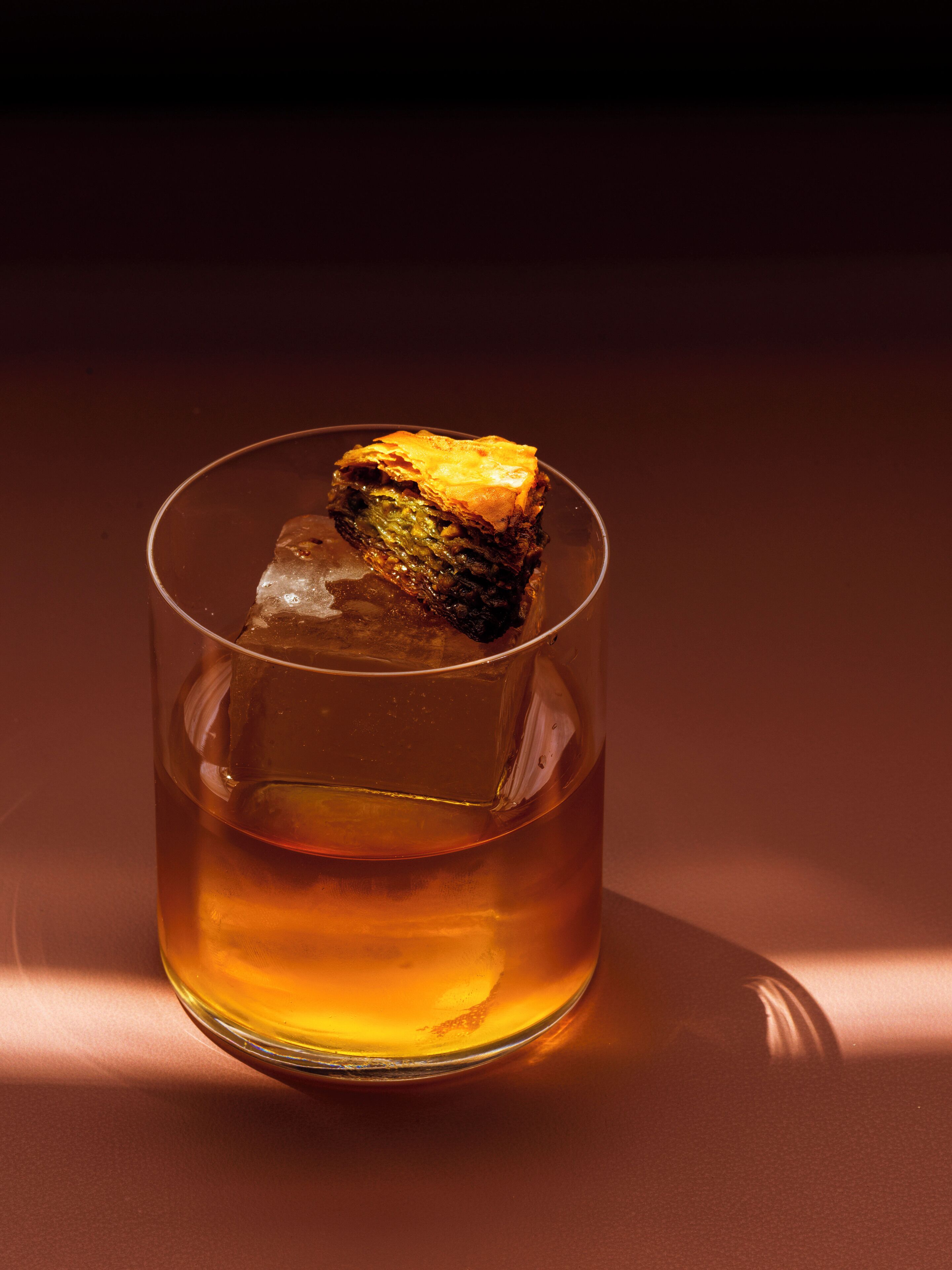 A clear glass with a golden liquid and a cube of ice.