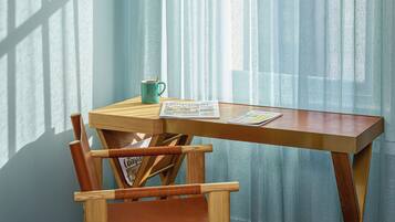 A wooden table with a magazine, a mug, and a chair in a room with light blue curtains.