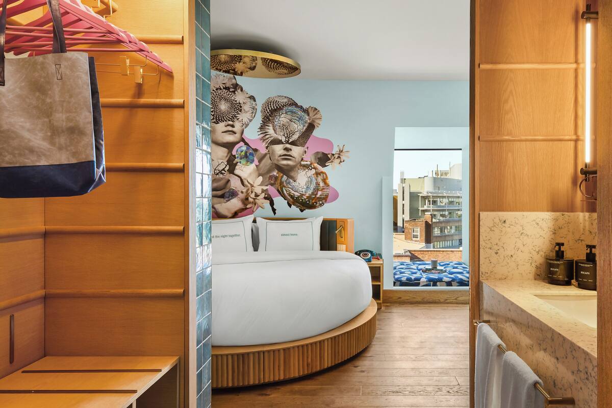 Een moderne badkamer met een rond bed, houten lambrisering, een grote spiegel en uitzicht op de stad door het raam.