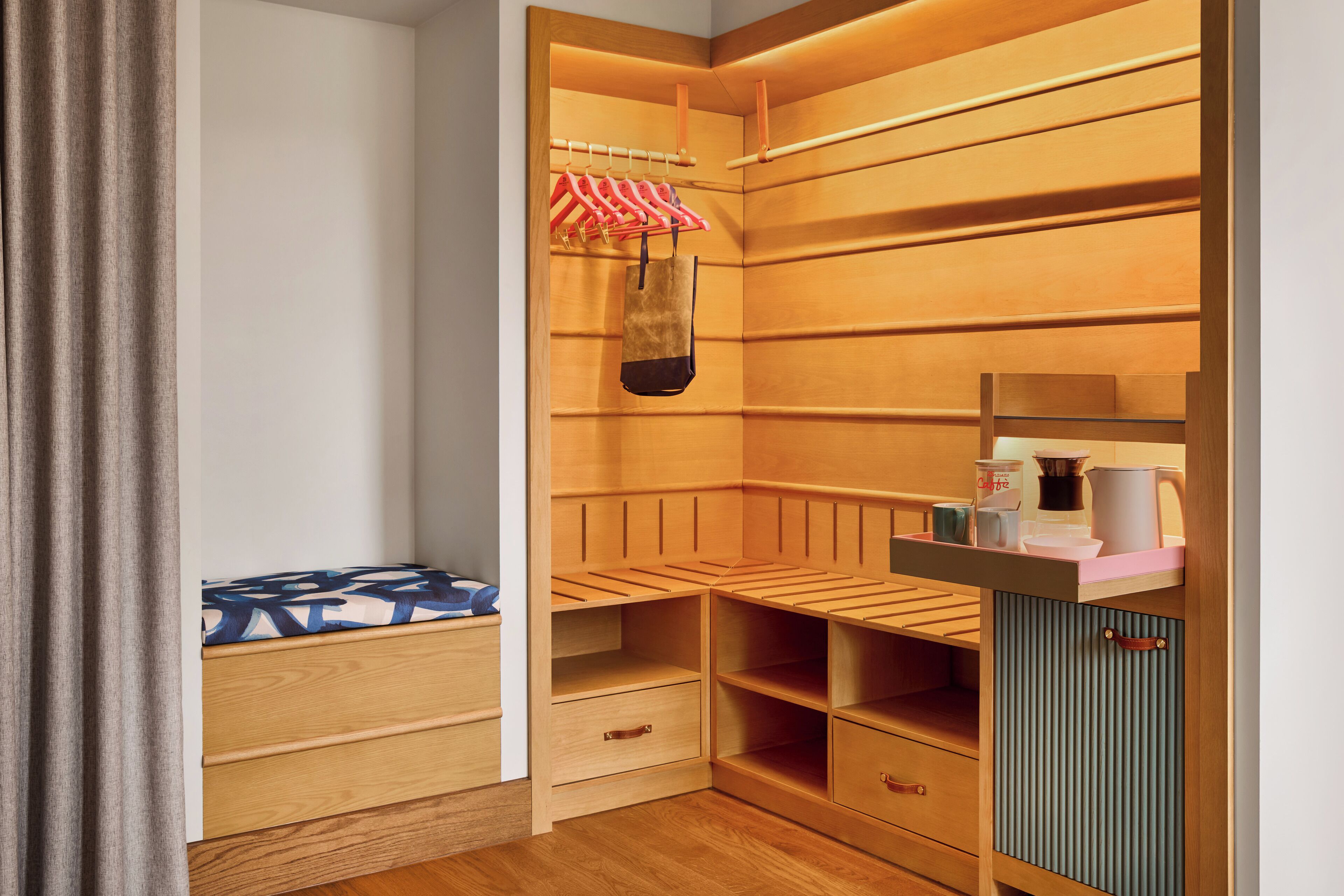 Un armario de madera con varios estantes y cajones, una barra para colgar ropa y un pequeño estante con una cafetera y otros objetos.