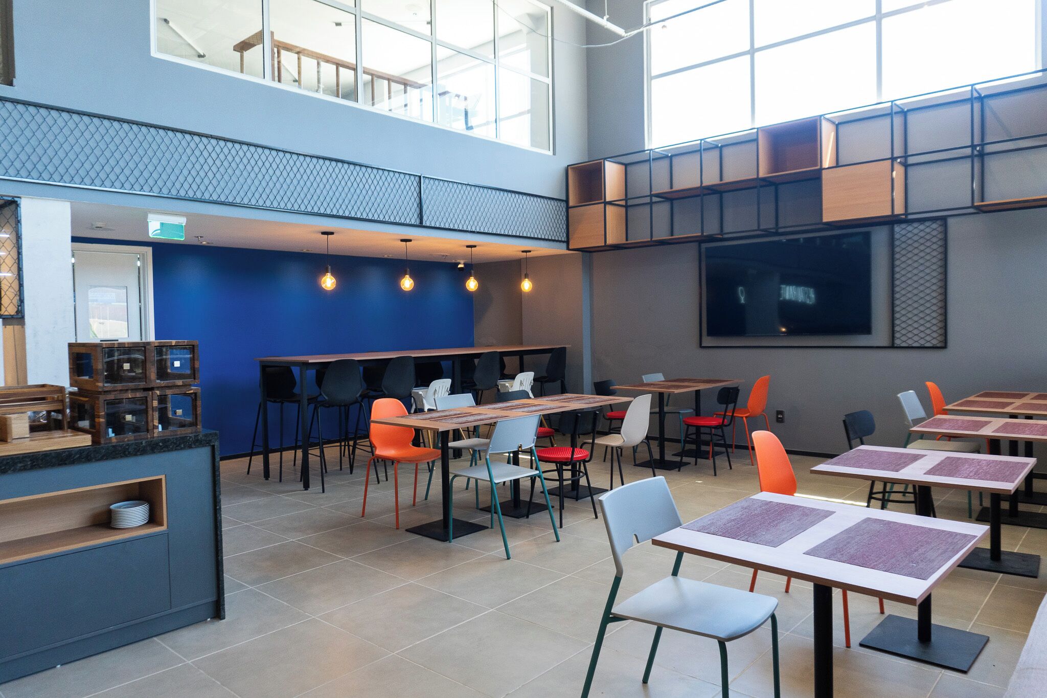 Una cafetería moderna con varias mesas y sillas, una barra con productos a la vista y grandes ventanales que dejan entrar luz natural.