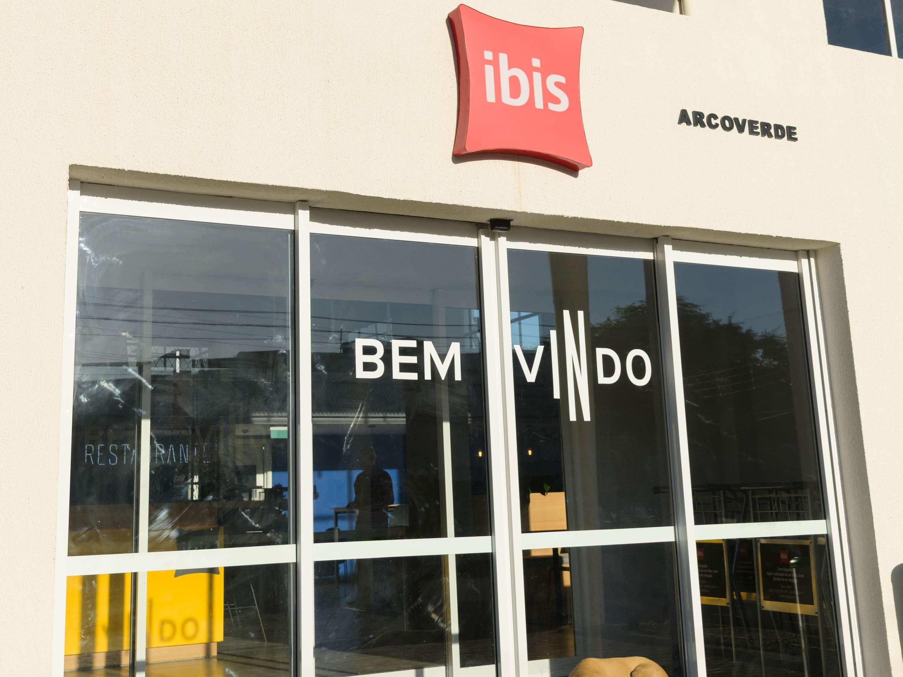 A storefront with a large glass window displaying the name 'BEM VINDO' and a red 'ibis' sign above.