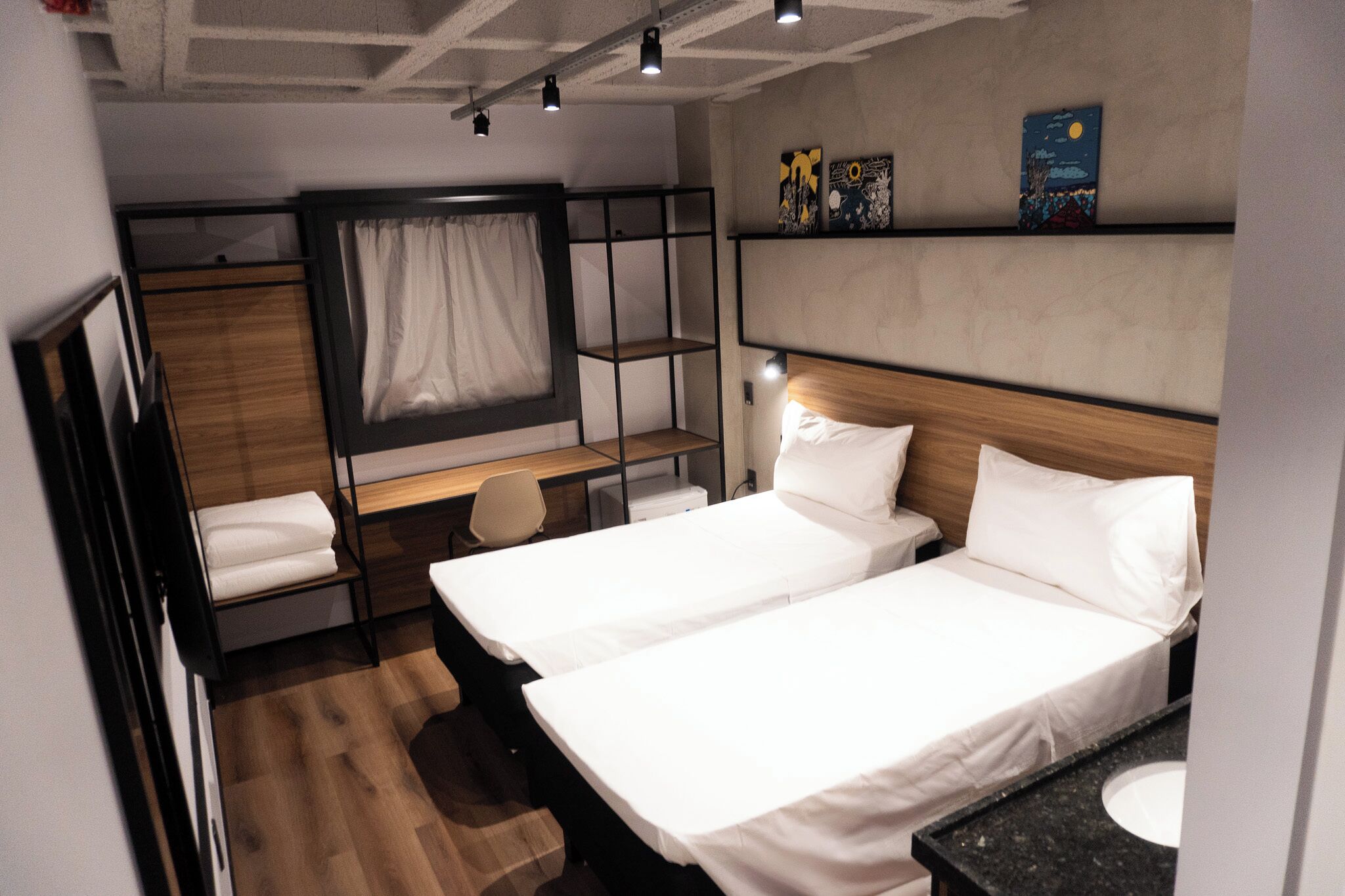 A compact hotel room with two beds, a desk, and a small seating area.