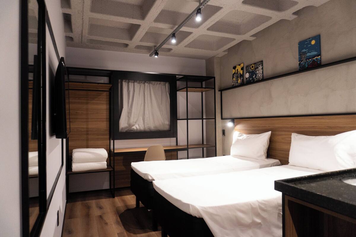 A modern hotel room with a bunk bed, a desk, and a bedside table.