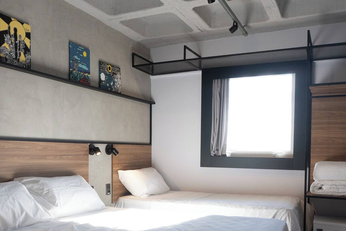 A modern hotel room with two beds, a large window, and a wooden headboard.