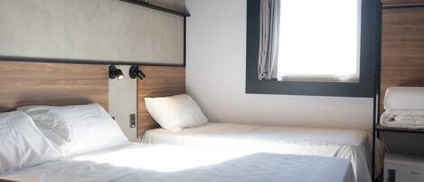 Una habitación de hotel moderna con dos camas, un ventanal grande y un cabecero de madera.