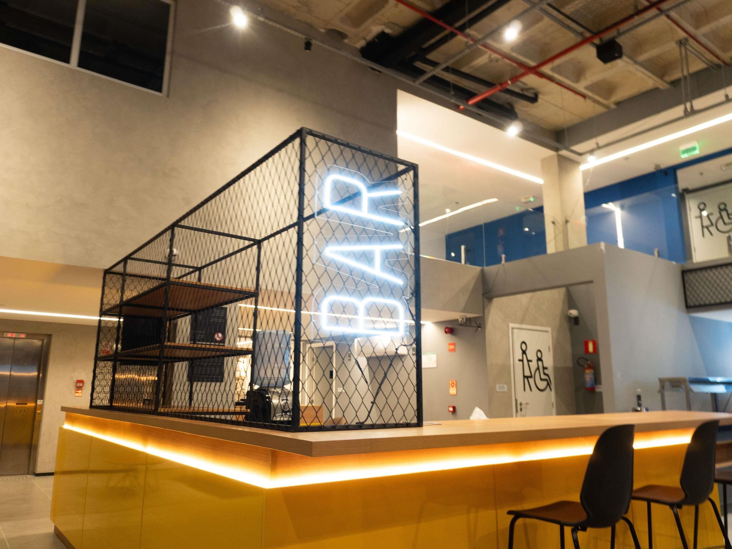 A modern bar area with a neon sign, seating, and a counter.