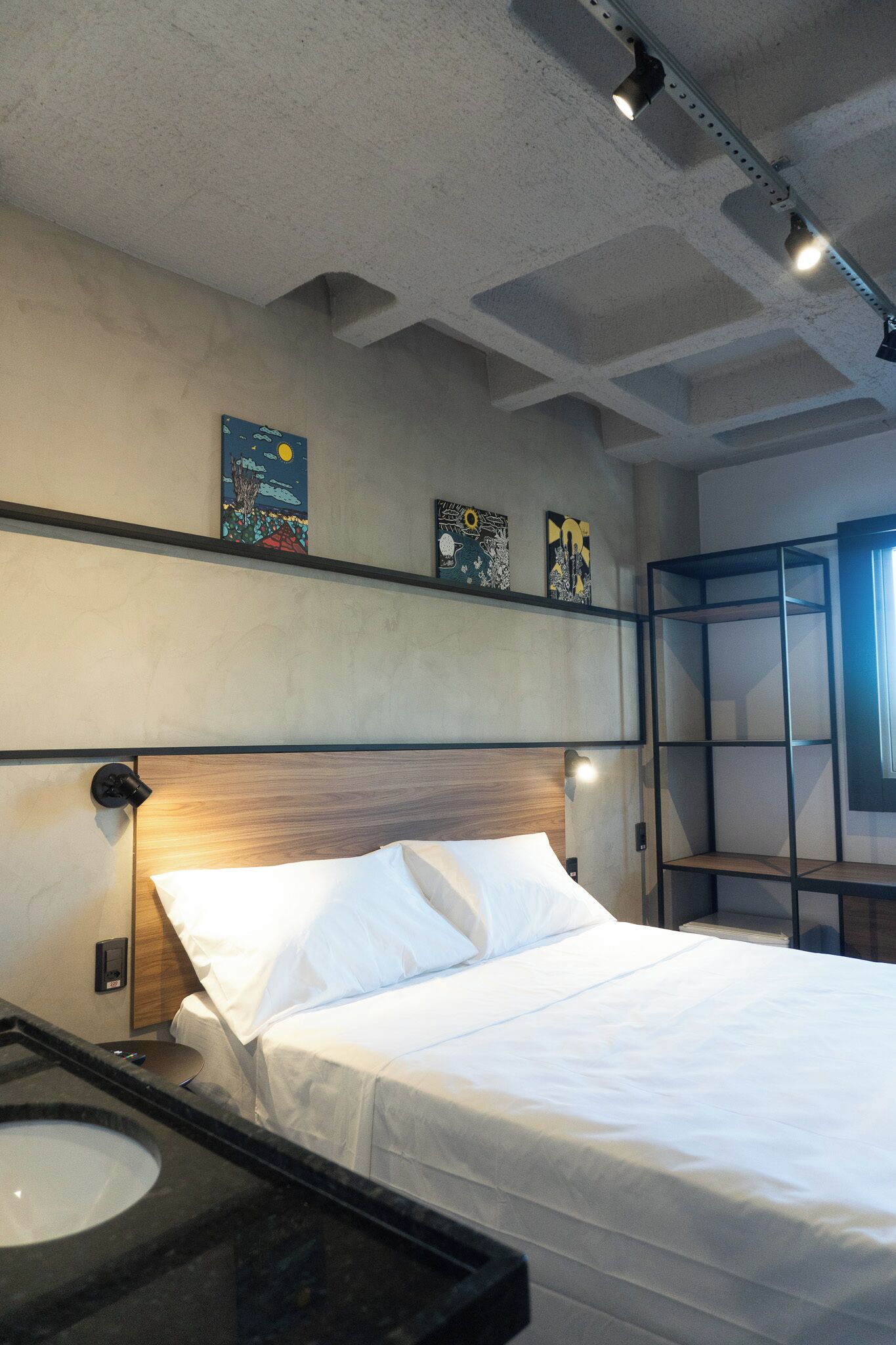 A hotel room with a bed, a nightstand, a mirror, and artwork on the wall.