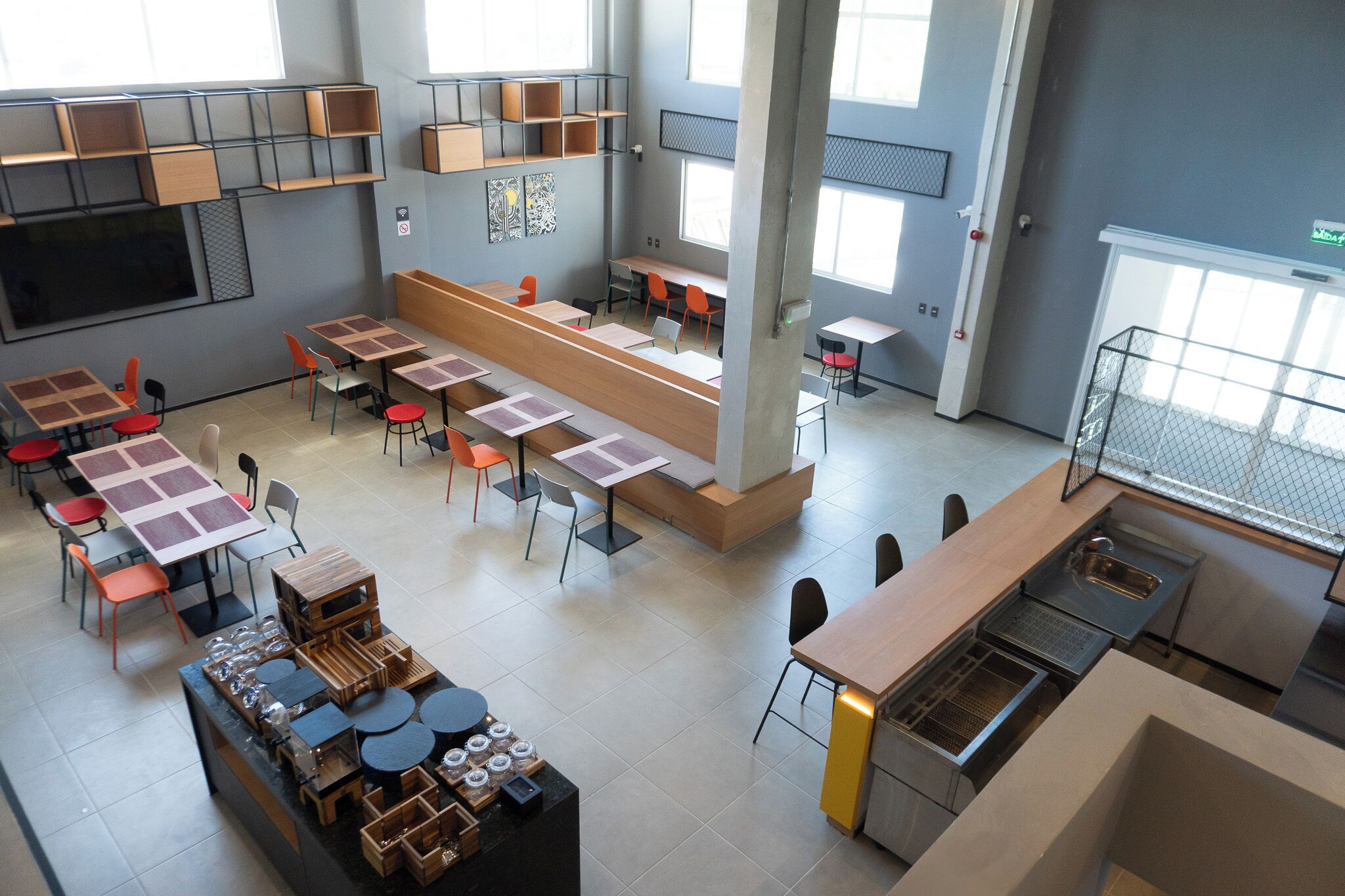 A modern classroom with multiple tables and chairs, a large screen, and a kitchen area with a sink and counter.