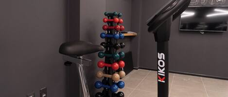A gym with a stationary bike, a wall-mounted TV, and a rack of colorful dumbbells.