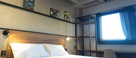A hotel room with a bed, a nightstand, a desk, and a window with curtains.
