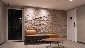 Eine moderne Lobby mit Steinwand, einer Couch mit Kissen, einem runden Tisch und einer Tür mit der Aufschrift 'MALERO'.