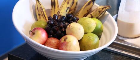 A bowl of assorted fruits including bananas, apples, and grapes on a countertop.