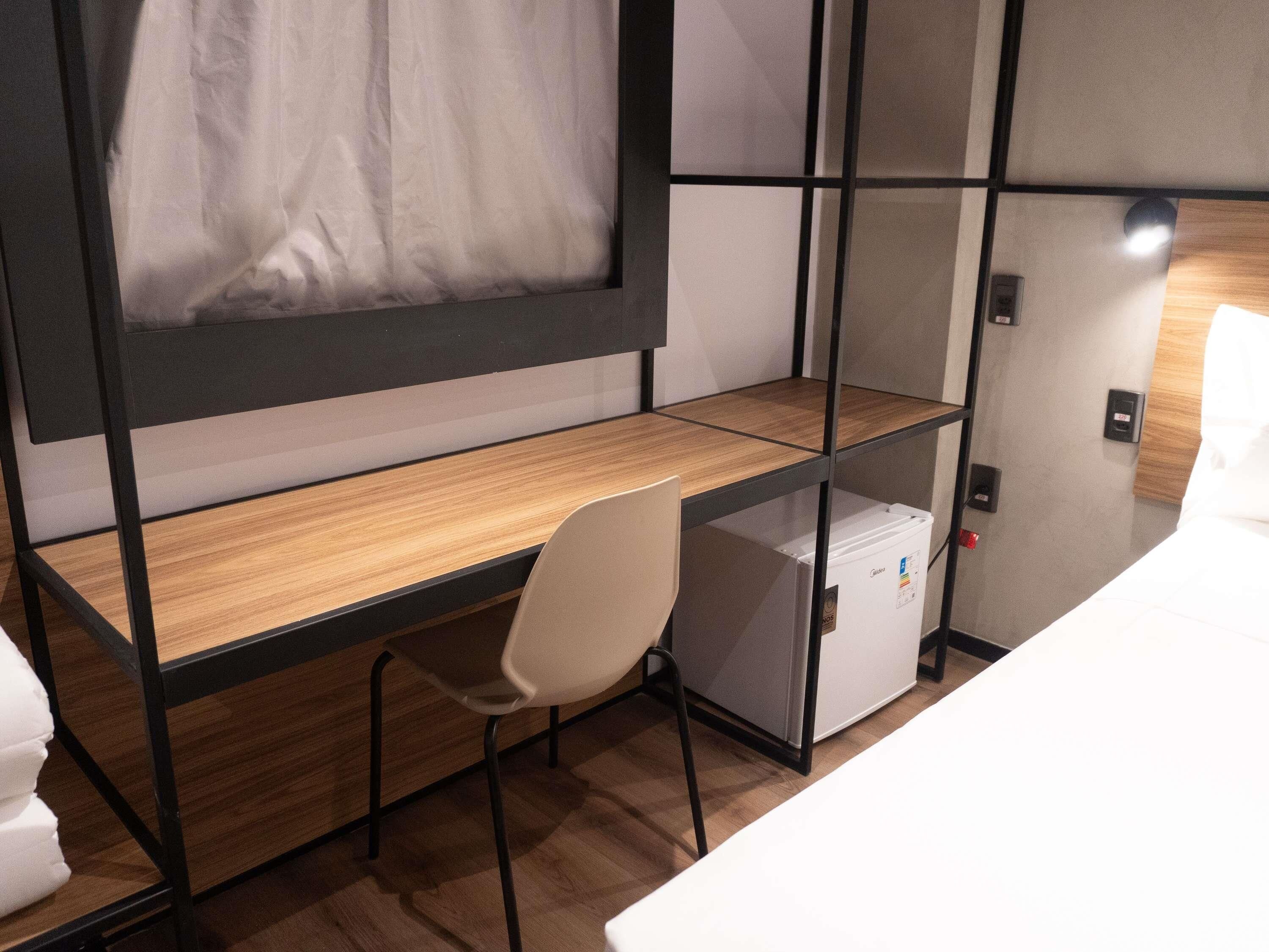 A compact room with a wooden desk, a chair, a white refrigerator, and a curtain.