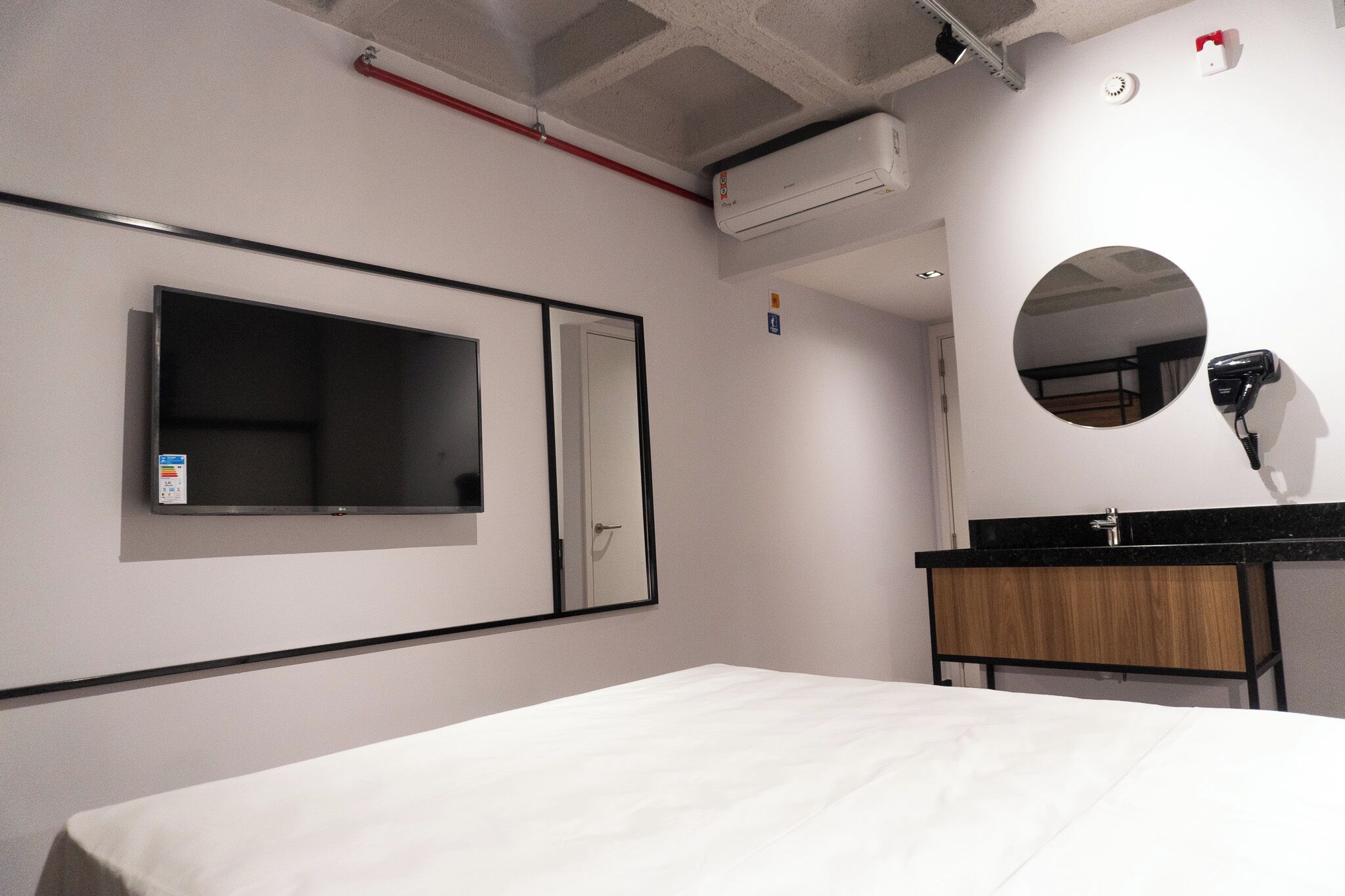 A hotel room with a bed, a flat-screen TV, a mirror, a hairdryer, and a wooden cabinet.