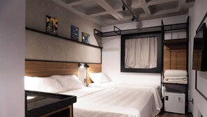 Ein Hotelzimmer mit zwei Betten, einer kleinen Küchenzeile, einer Decke mit freiliegenden Balken und einem Fenster mit Vorhängen.