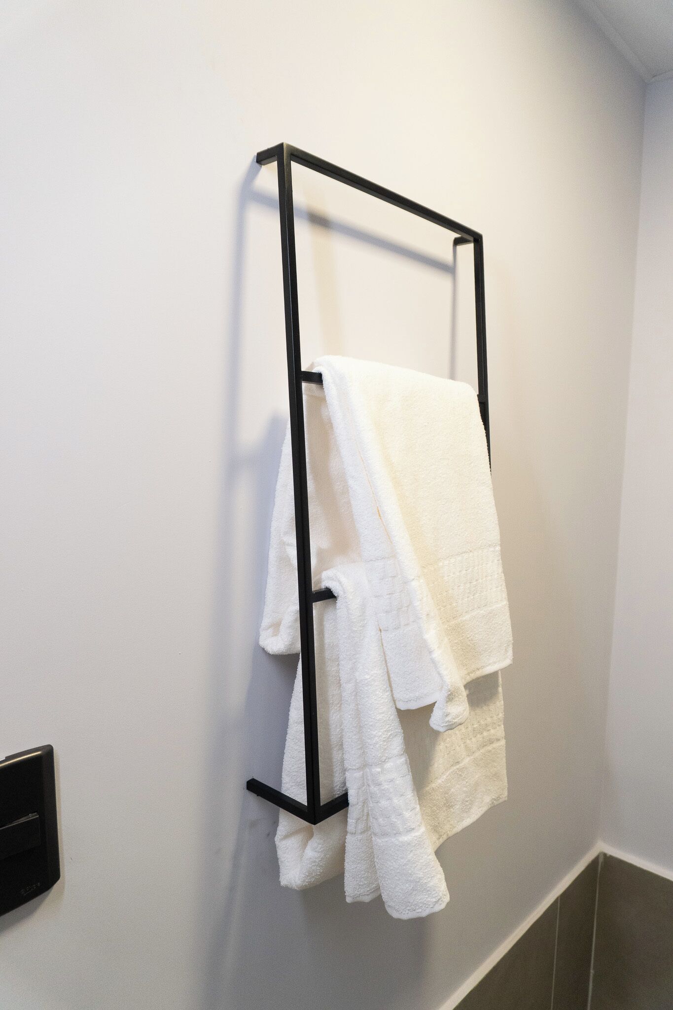 Ein schwarzer Handtuchhalter mit zwei weißen Handtüchern, an einer weißen Badezimmerwand befestigt.