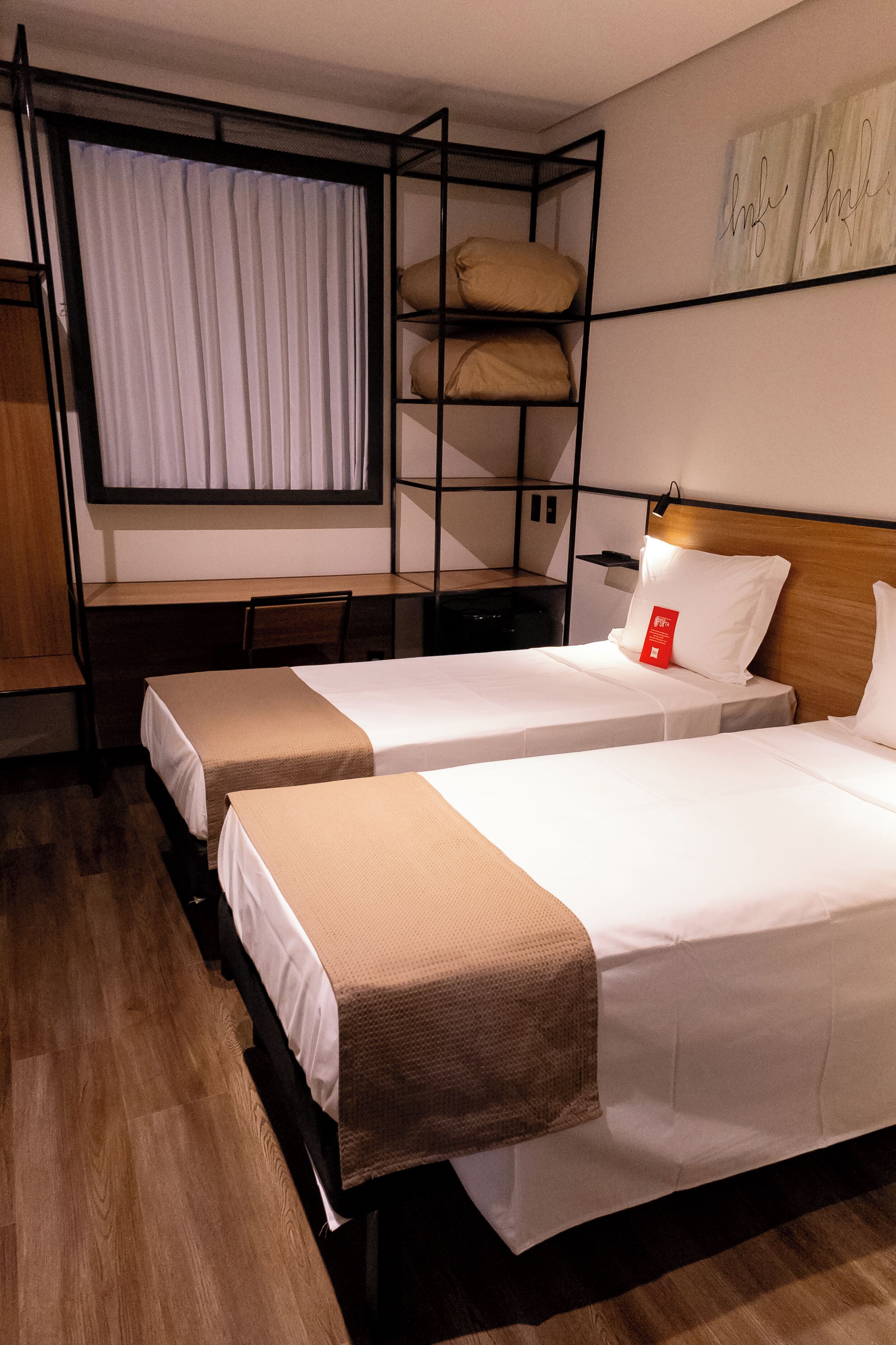 A hotel room with two beds, a bunk bed above, a desk, and a window with curtains.