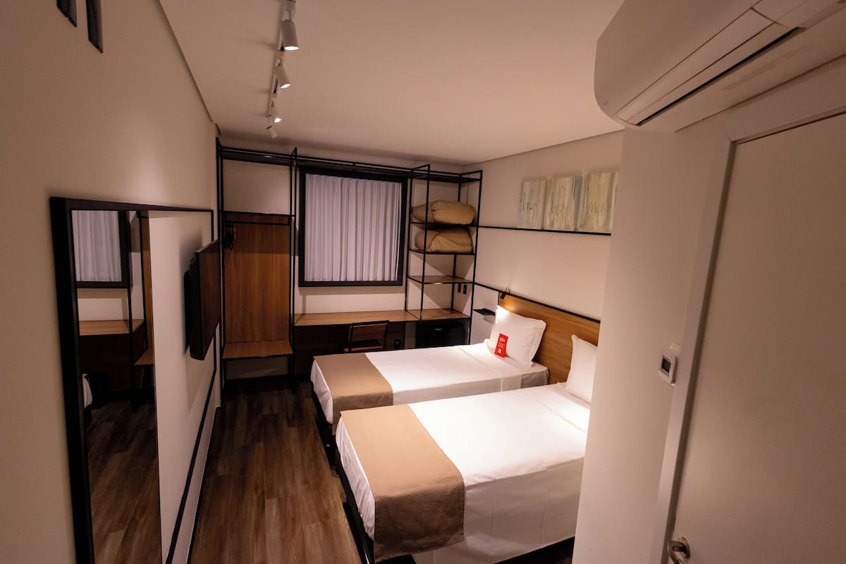 A hotel room with two beds, a desk, a chair, a wardrobe, and a window with curtains.