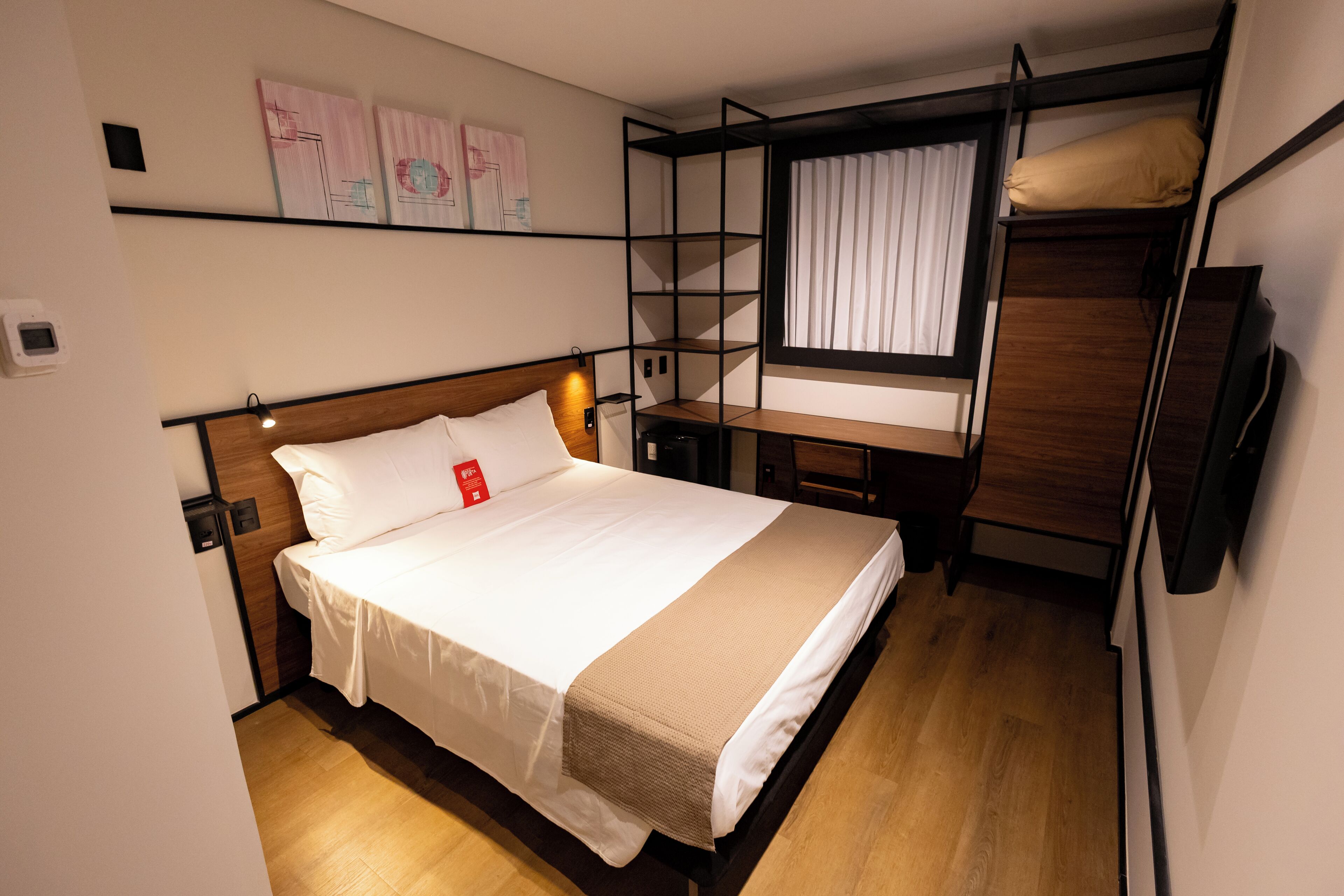Habitación de hotel pequeña con literas, una cama individual, un escritorio y una ventana con cortinas.
