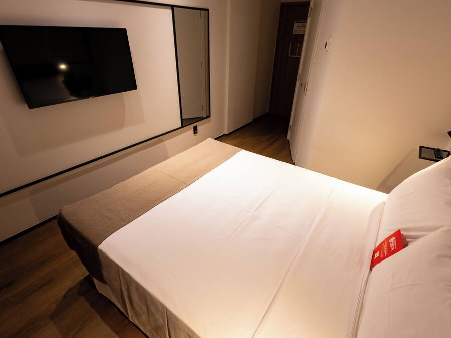 A hotel room with a bed, a flat-screen TV mounted on the wall, and a wooden floor.