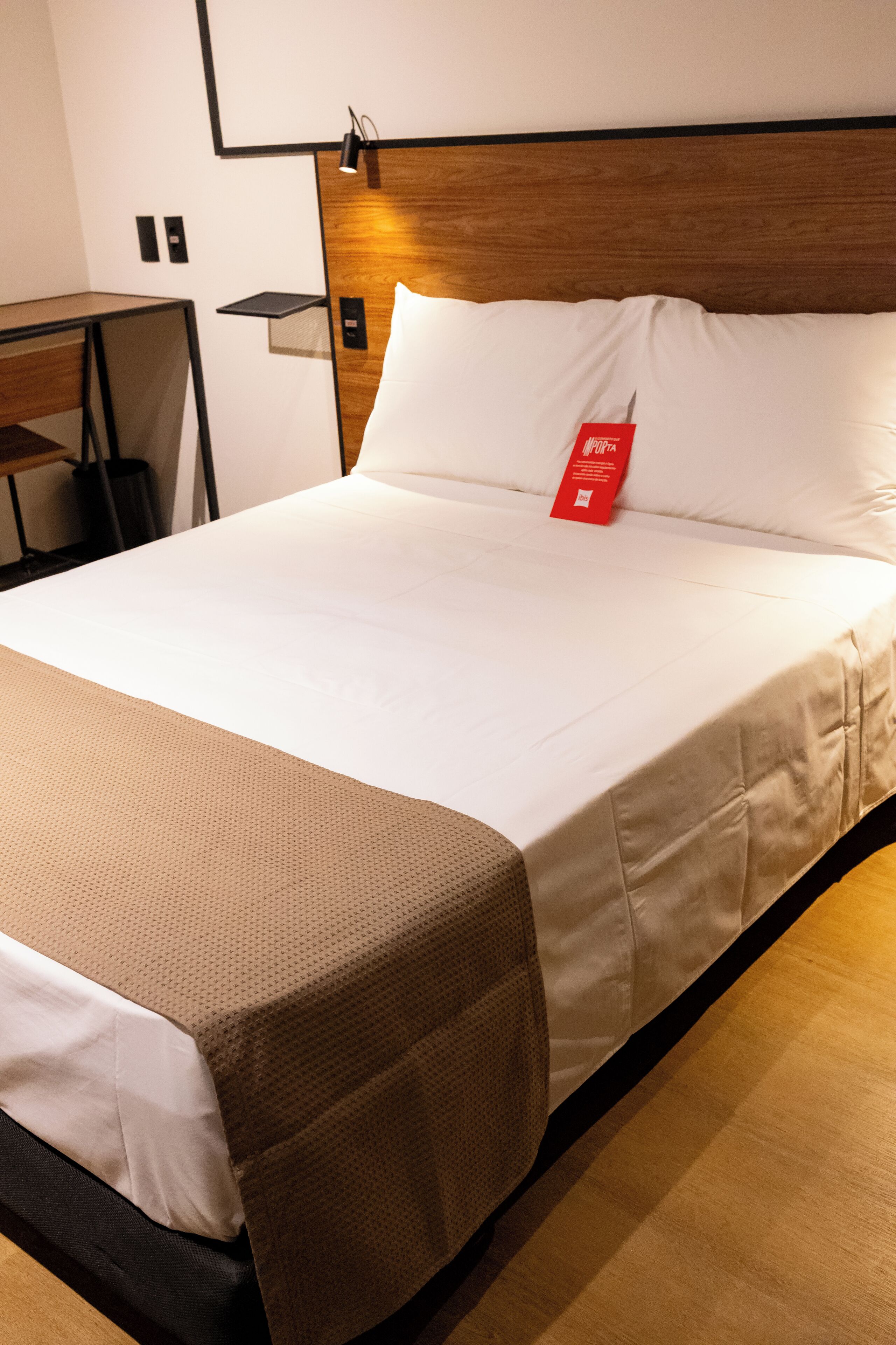 Ein ordentlich bezogenes Bett mit einer weißen Matratze, einer braunen Decke und einem roten Etikett auf dem Kopfkissen.