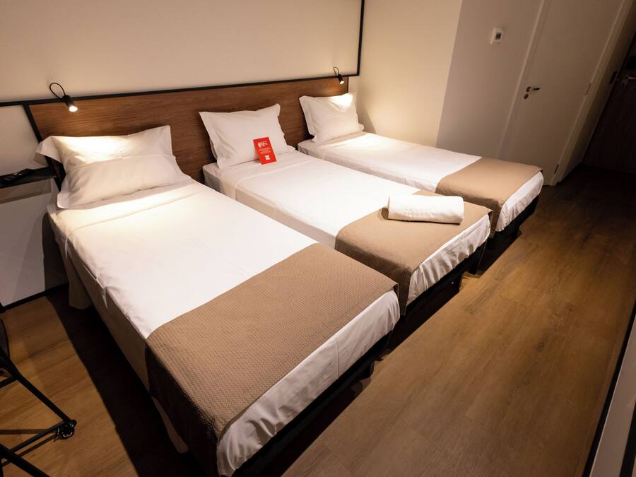 Una habitación de hotel con dos camas individuales, un cabecero de madera y una mesita de noche con lámpara.
